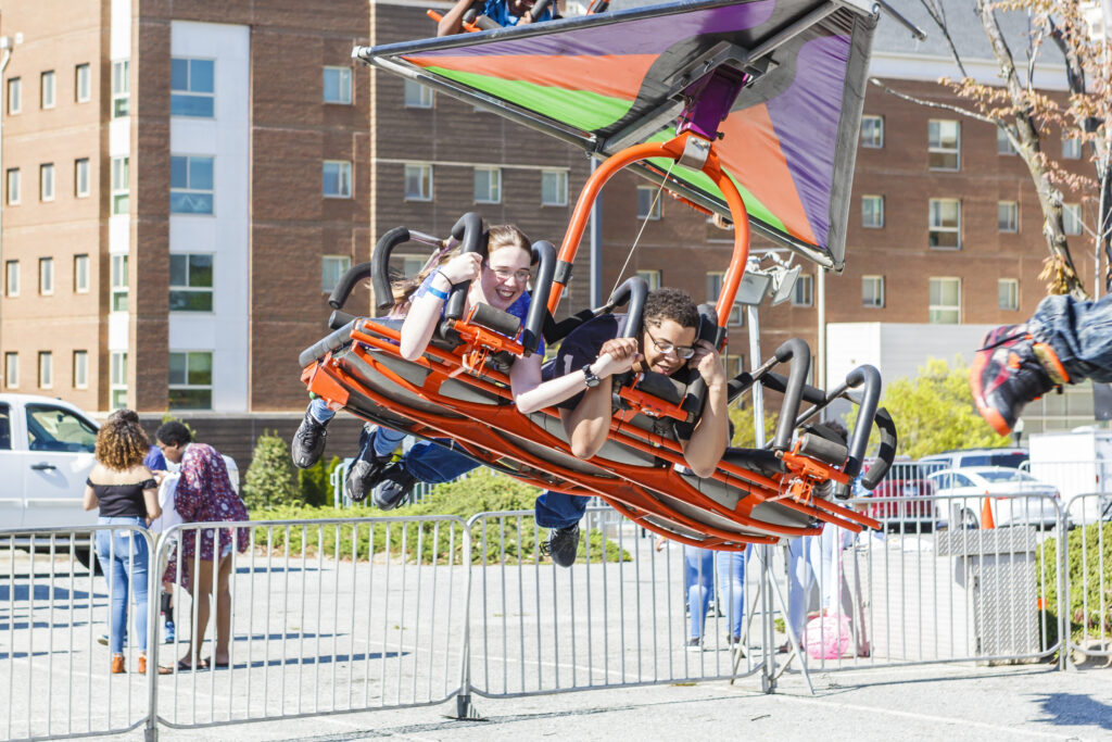 Two students laying horizontally on a flying carnival ride.