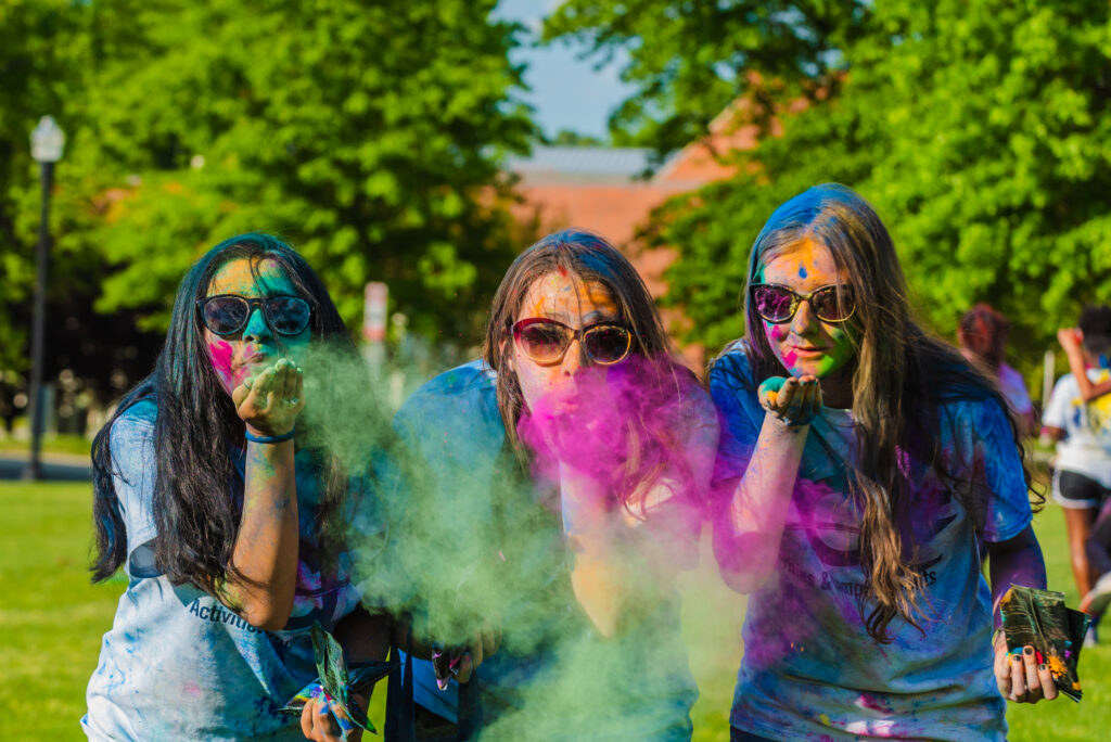 Three students with sunglasses blowing colorful powder off of their hands.