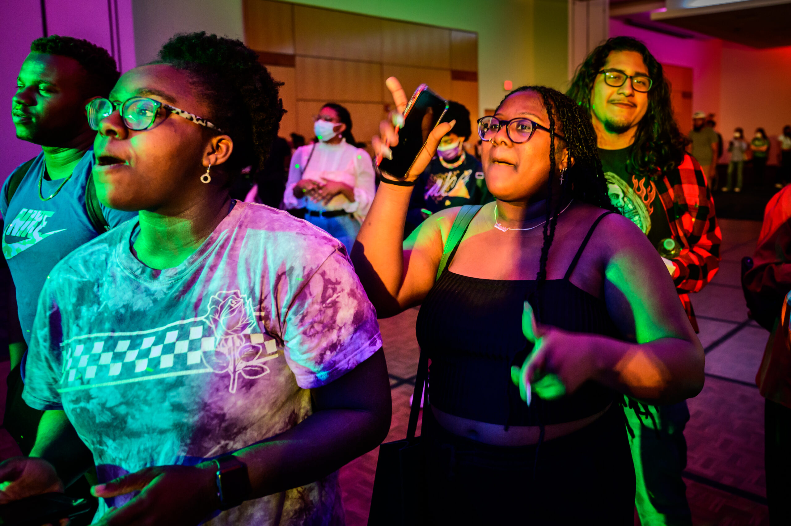 A diverse group of students dancing inside a dark ballroom with colorful lights.