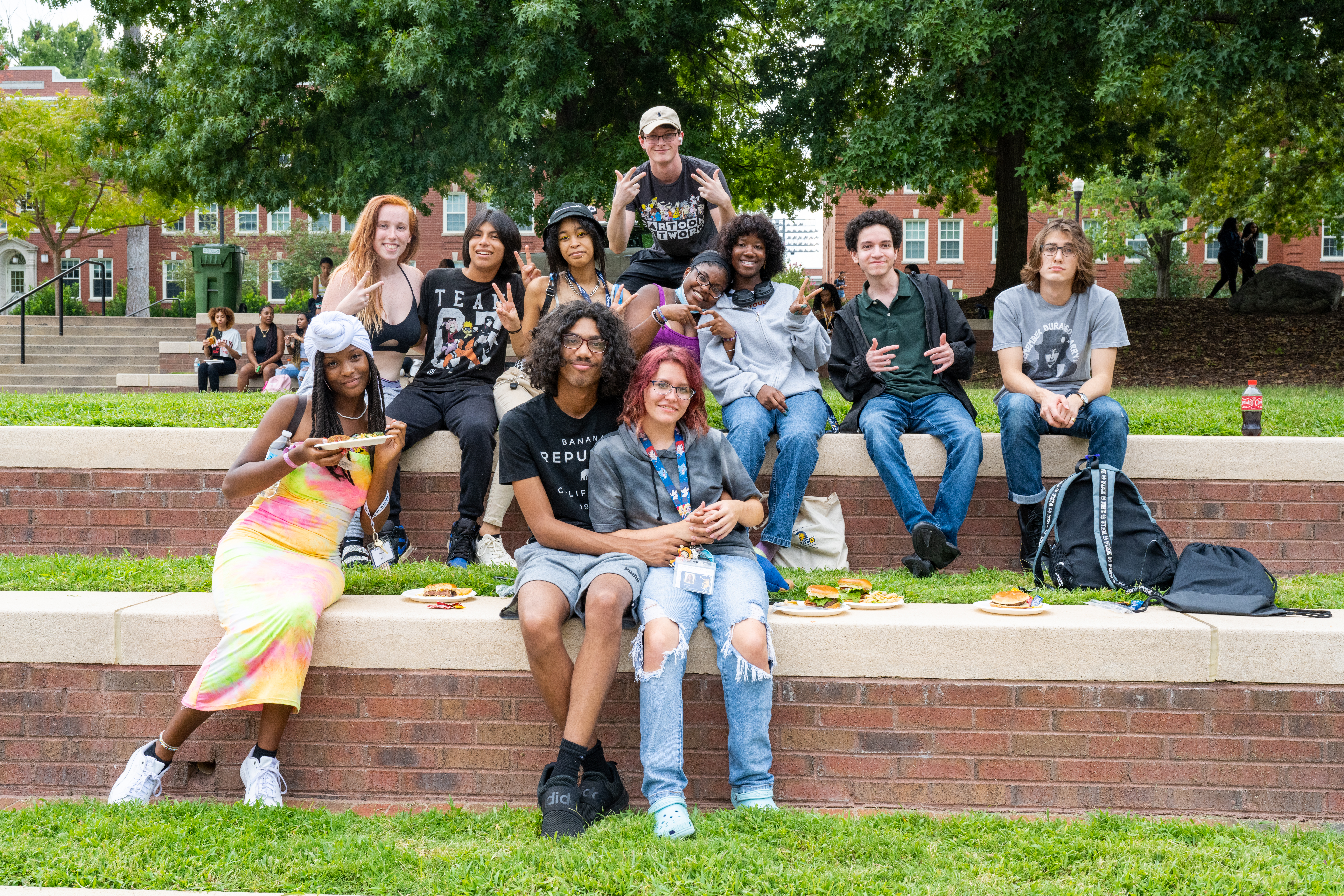 A diverse group of students sitting outside on the grass with plates of food smiling at the camera.