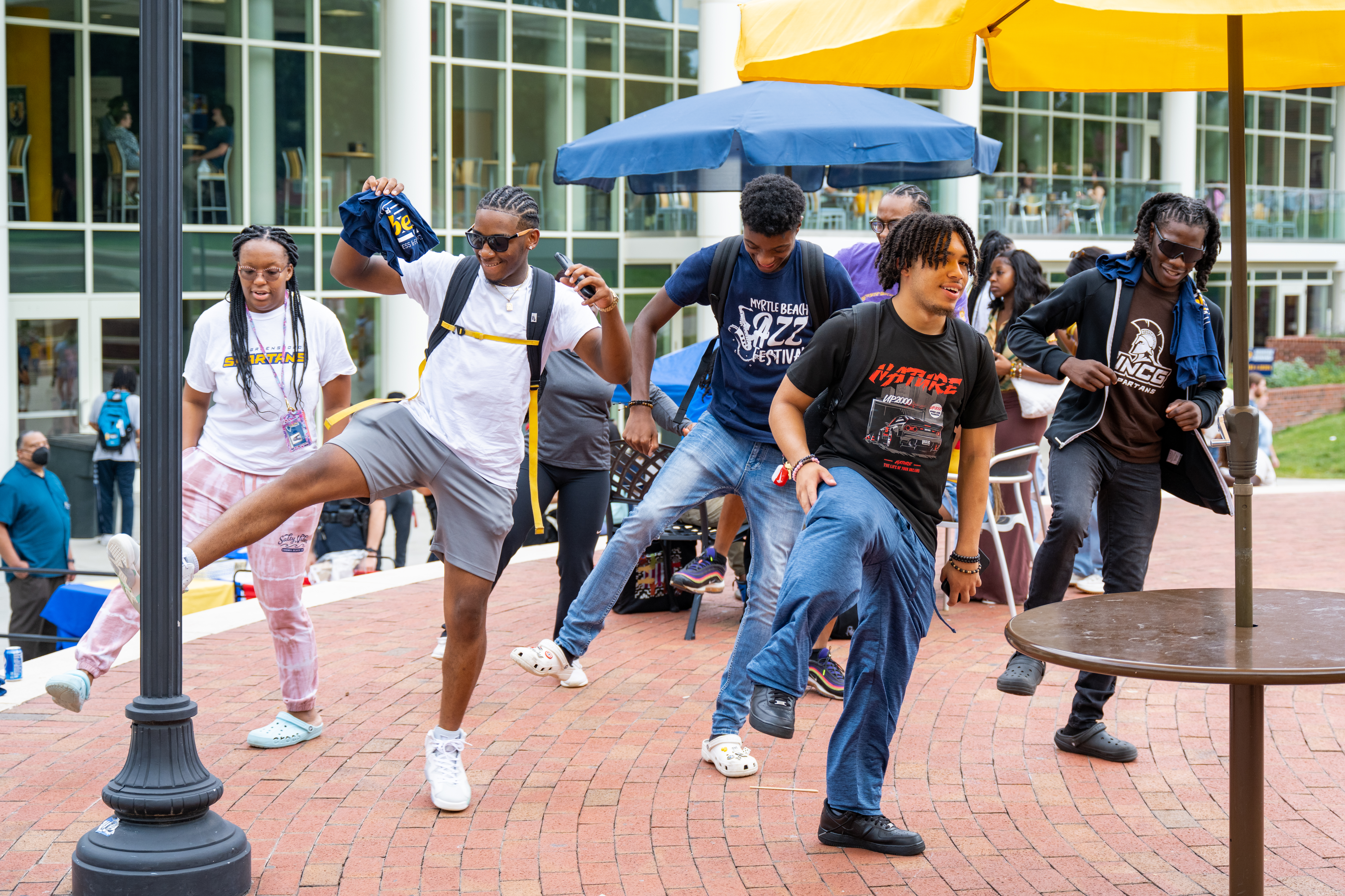 A group of students dancing outside near tables with umbrellas.