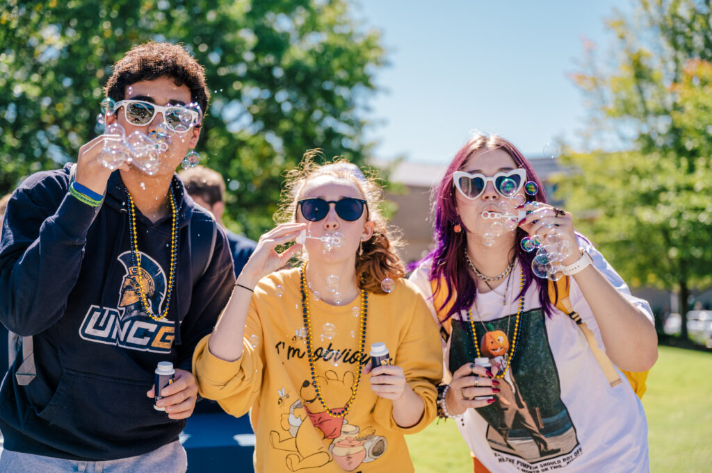 Three students wearing sunglasses outside blowing bubbles.
